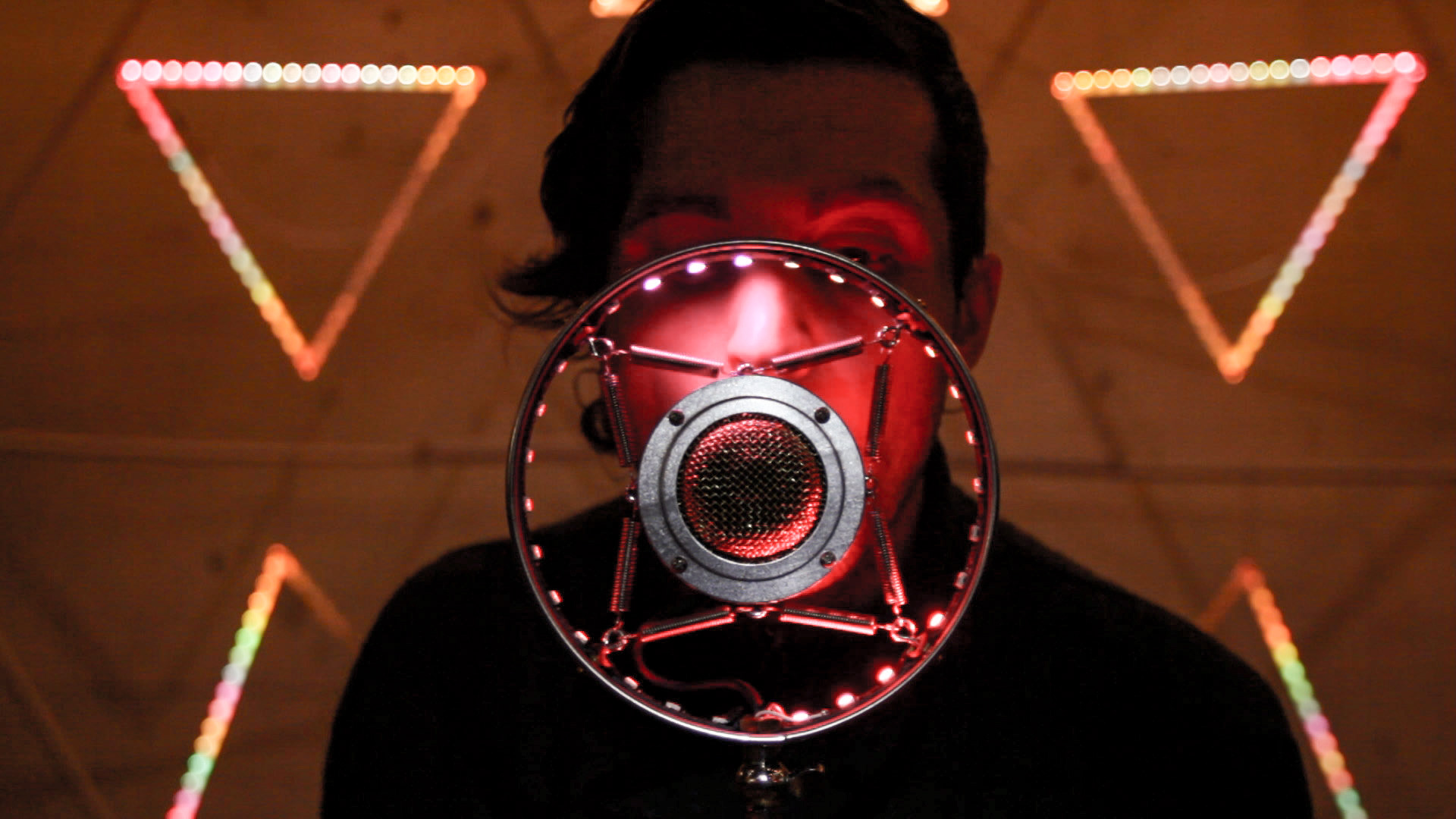 Myles de Bastion lit in deep red, speaking into a ring-shaped microphone