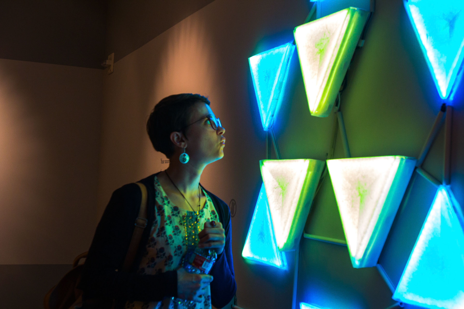 A visitor in profile lit by large glowing triangular panels arranged as a star