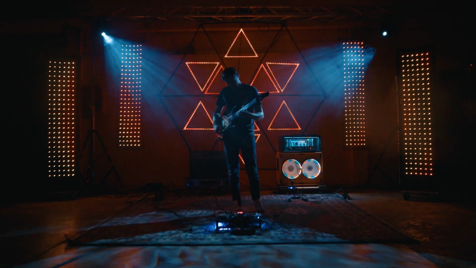 Wide stage view with illuminated triangles behind the performer