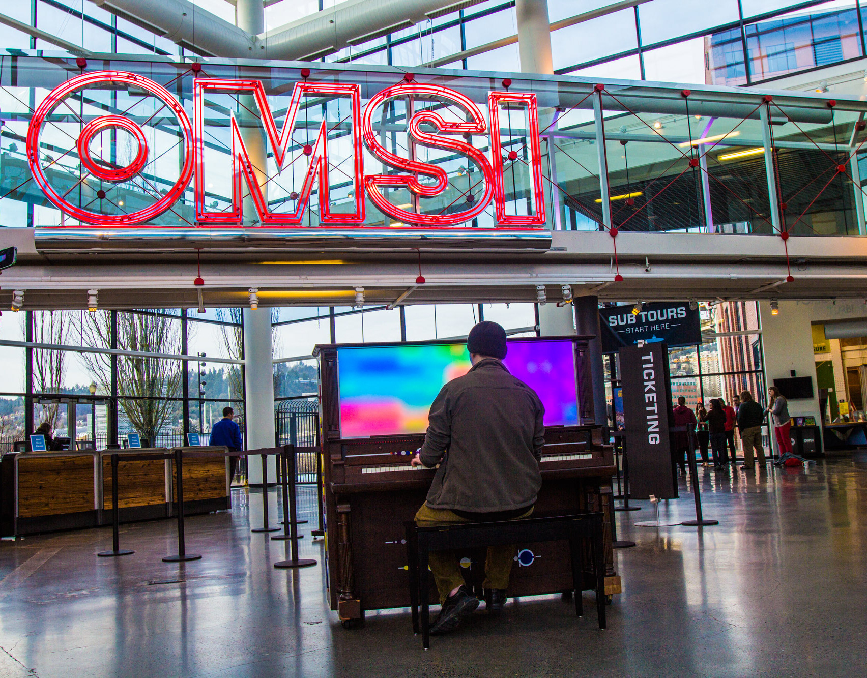 A visitor plays the LED piano in the atrium of the Oregon Museum of Science and Industry beneath a large OMSI sign